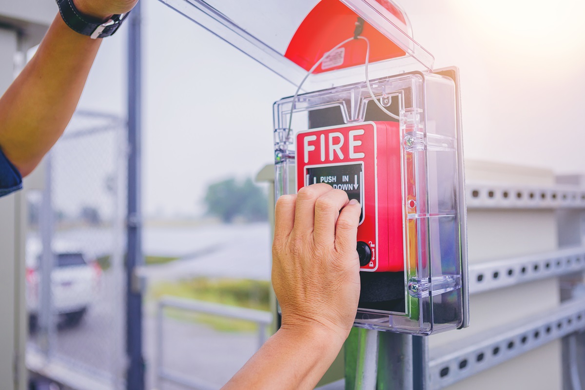 Electrical technician hands open and pushing fire alarm switch at solar panel plant.